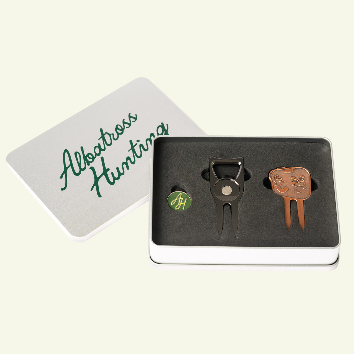 Albatross Hunting ball marker tin at an angle with the lid set aside, marker and two divot tools in foam
