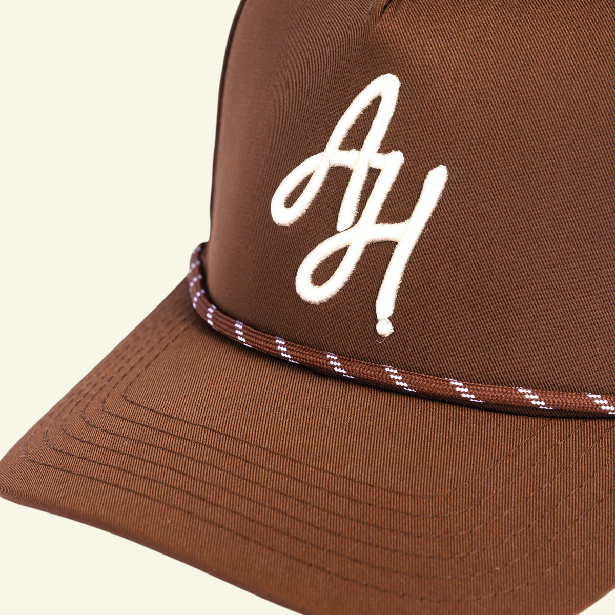 Close-up of white AH embroidery and brown and white braided rope on a brown golf cap