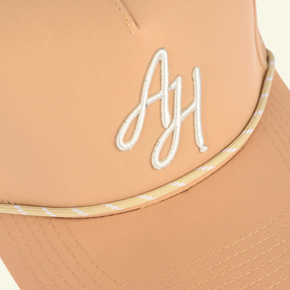 Close-up of white AH script embroidery and tan/cream rope on a tan golf cap